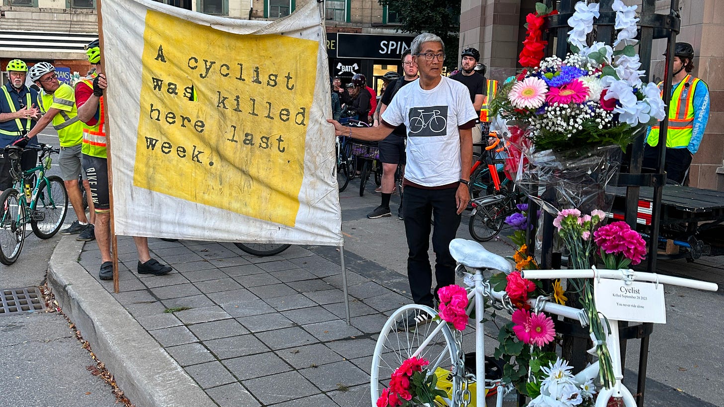 Participants in a memorial ghost ride for an unknown 76 year old cyclist placing a ghost bike at the corner of James Street North and York Boulevard on October 6, 2023