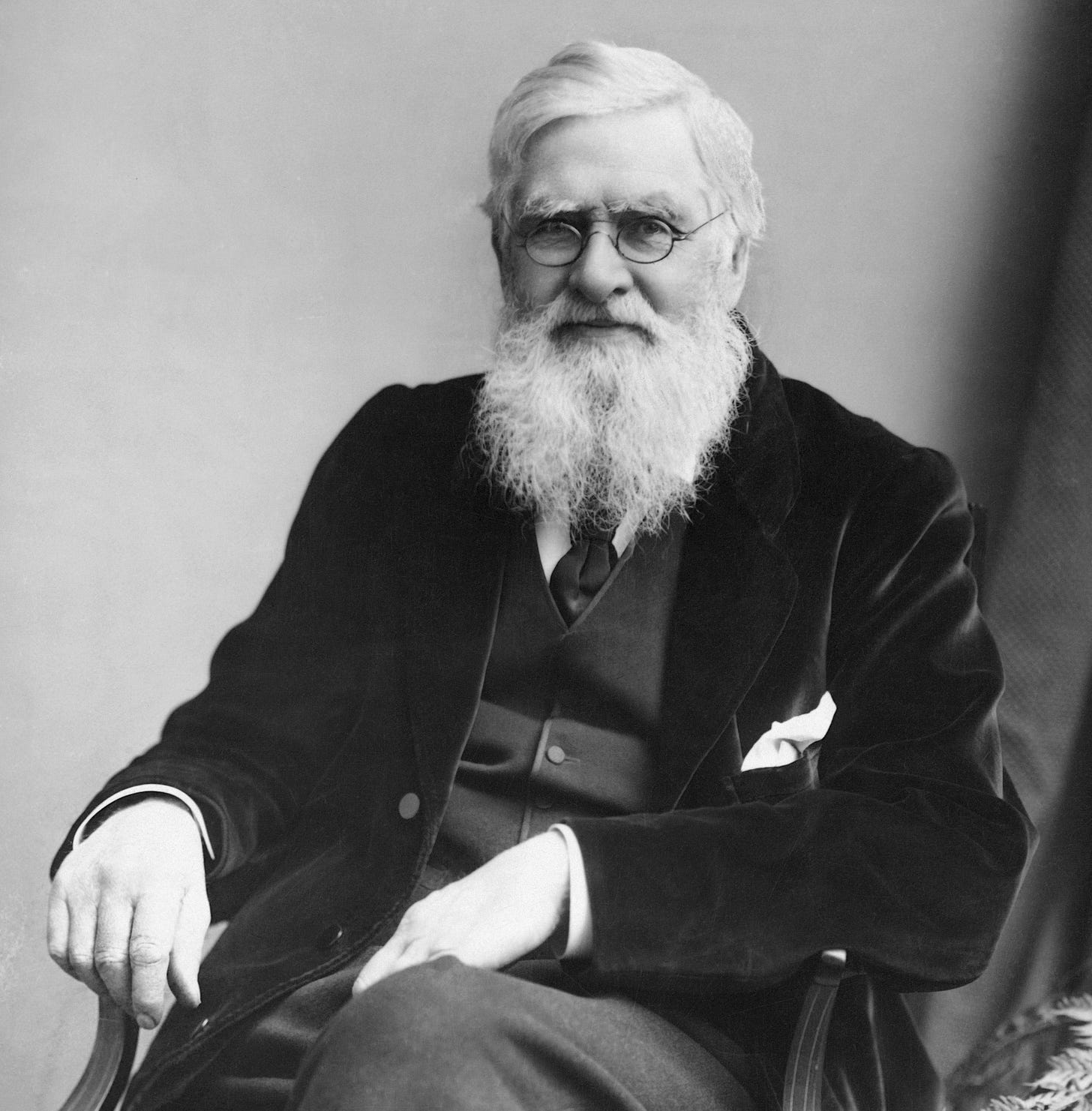 Elderly man with a long white beard, seated in a three-piece suit and glasses, looks at the camera. Elderly man with a long white beard, seated in a three-piece suit and glasses, looks at the camera.