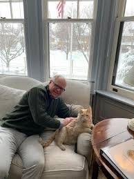 Governor Tim Walz with his cat on the couch, he's smiling, the cat looks mildly pleased as cats do