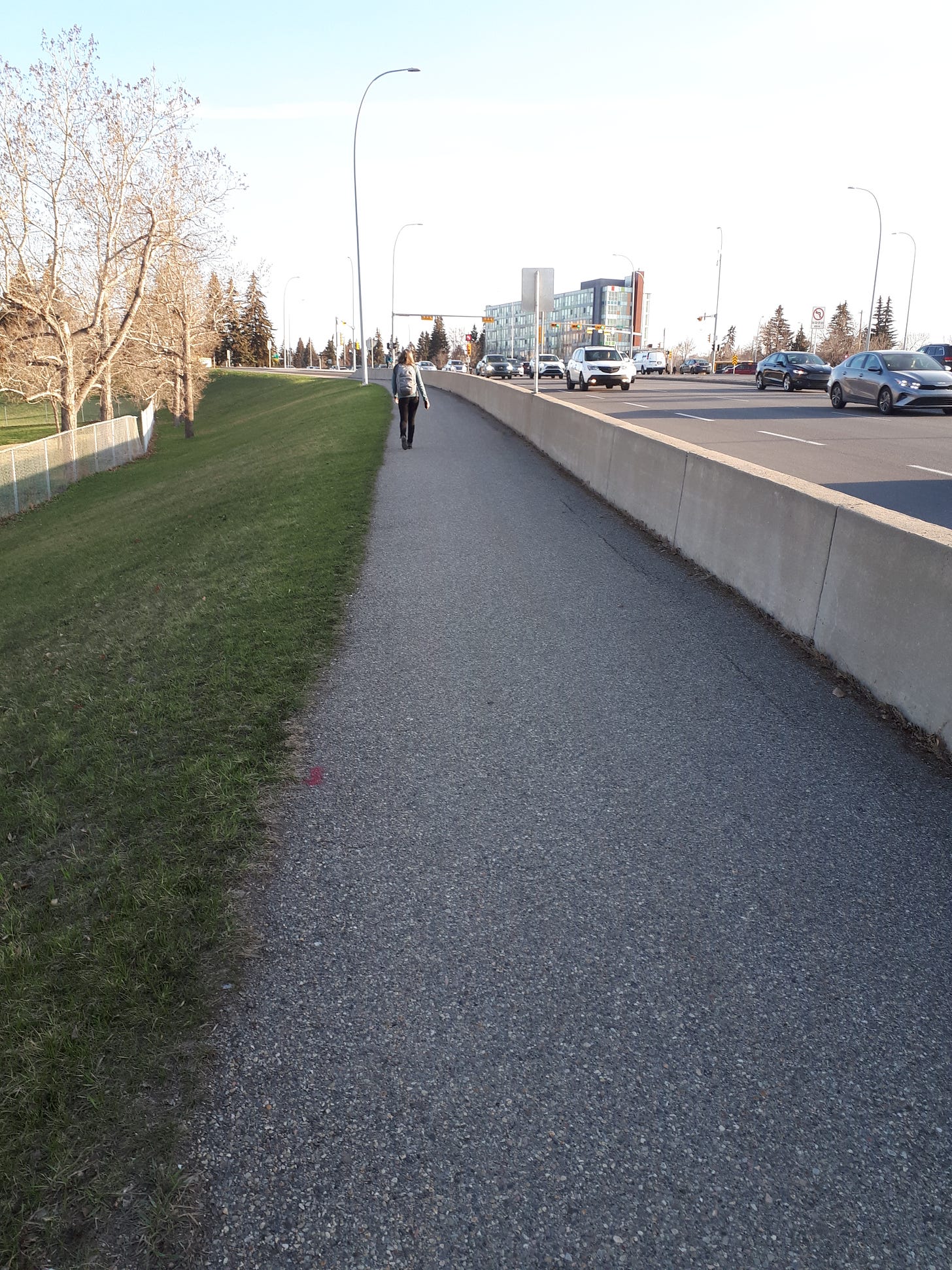 Woman walking on a trail beside a busy highway.