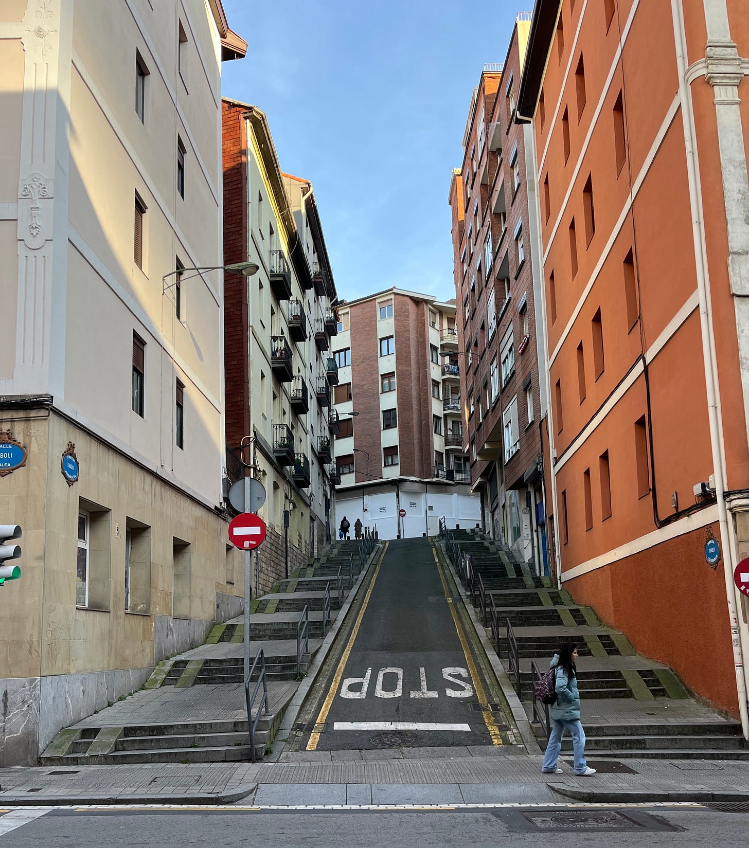 narrow steep road flanked by two very wide sets of stairs. People walking. 