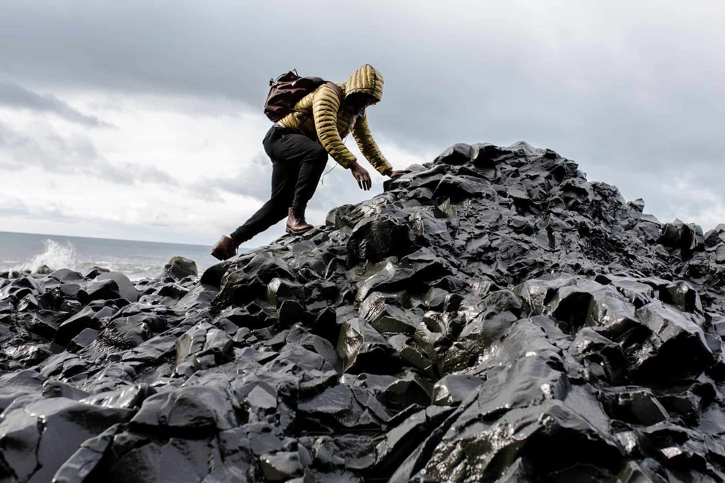 man wearing hoodie and black pants climbing up pile of rocks