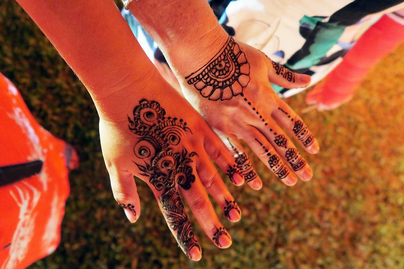 Two people hold out hands covered with henna.