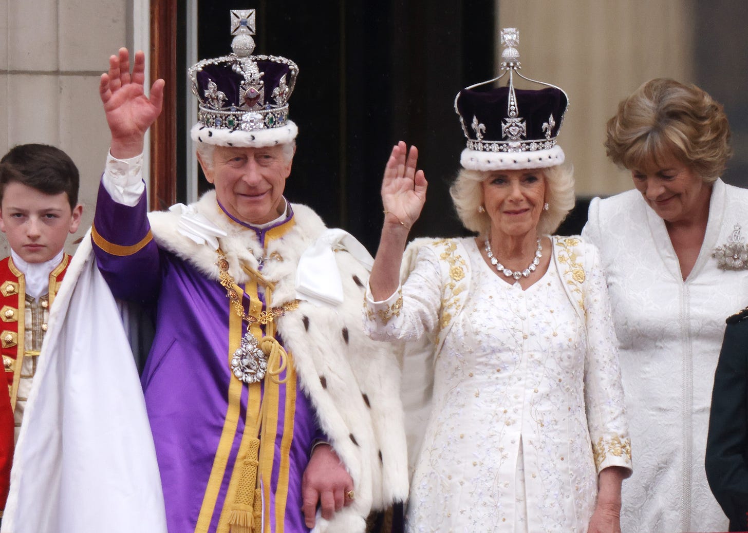 King Charles and Queen Camilla waving from balcony of Buckingham Palace wearing crowns