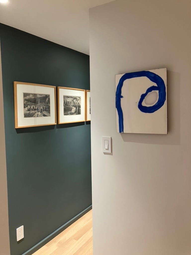 blue and white plexiglas art work on wall, flanked by green hallway with three Homers on wall