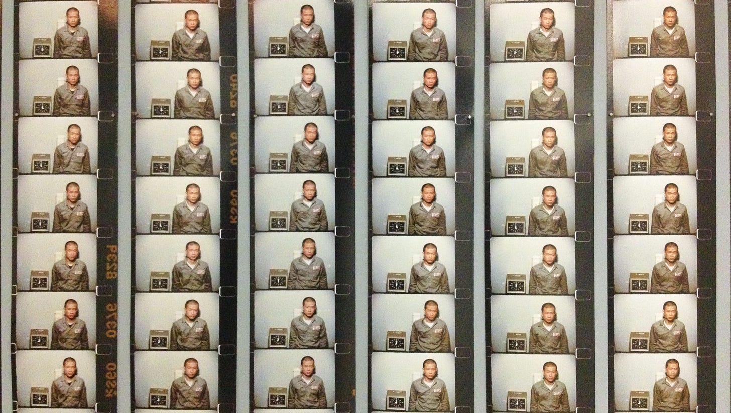 Techching Hsieh’ Time Clock piece - a close up of a film strip of images of a Hsieh with a shaved head with a time clock or punch clock on his right, he is wearing a workers jumpsuit in a greenish gray color