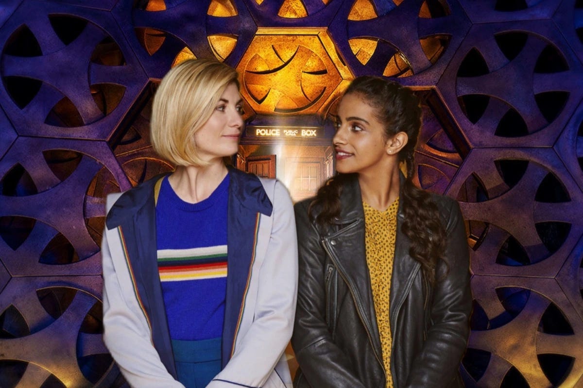 This image shows the Thirteenth Doctor (played by Jodie Whittaker, left) and Yasmin "Yaz" Khan (played by Mandip Gill, right) standing side-by-side inside their TARDIS. Both characters, with their hands folded in front of them, look at one another and smile. This image shows the Thirteenth Doctor (played by Jodie Whittaker, left) and Yasmin "Yaz" Khan (played by Mandip Gill, right) standing side-by-side inside their TARDIS. Both characters, with their hands folded in front of them, look at one another and smile.