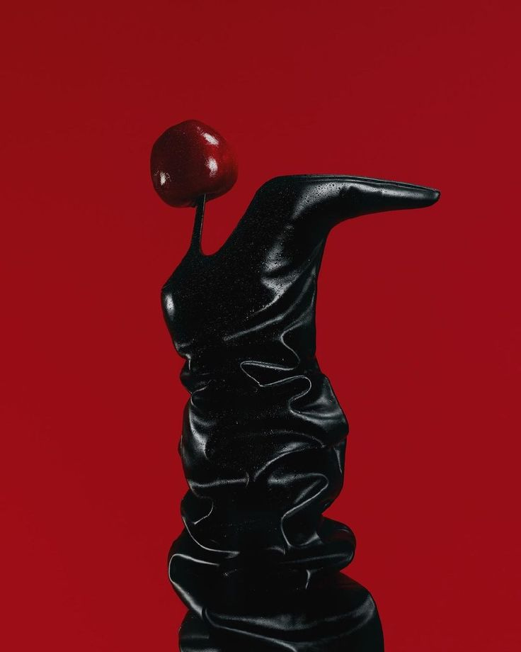 This may contain: a black sculpture with a red apple on it's head in front of a red background