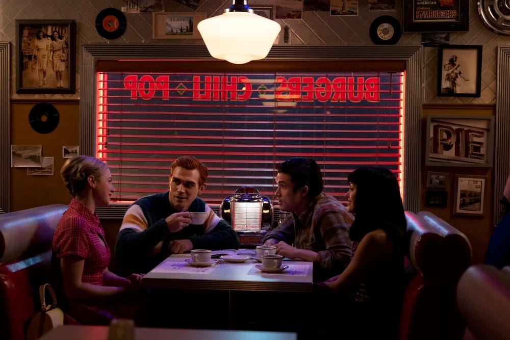 Betty, Archie, Reggie and Veronica sitting in a booth at Pop's.