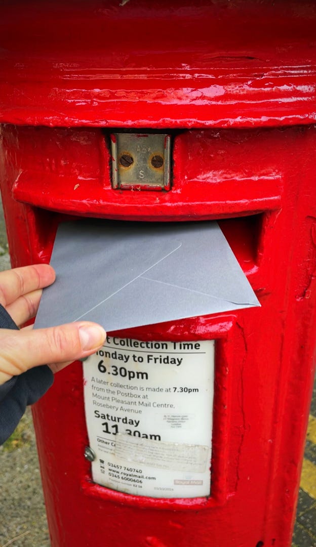 Close up of a UK red letterbox with a hand holding an envelope and posting it