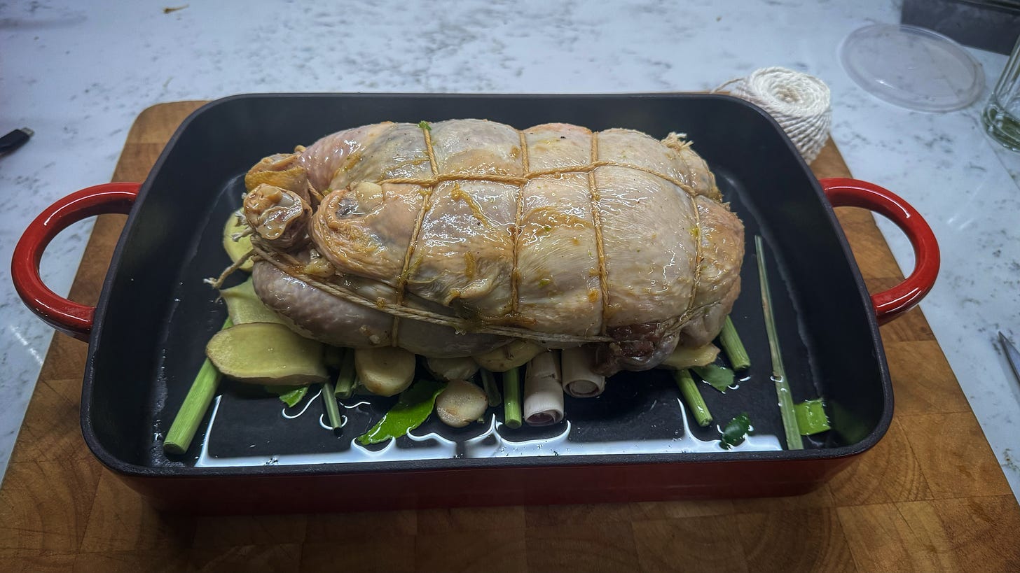 The boneless chicken now rolled and trussed, placed in a roasting pan on a bed of aromatic vegetables.