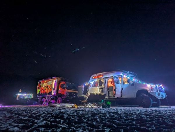 three trucks lined up on a dark sandy beach, all decked out with colorful holiday lights