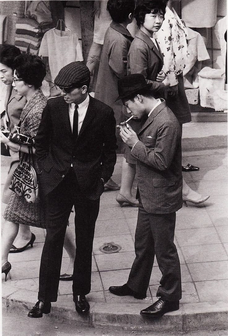 This may contain: an old black and white photo of people standing on the sidewalk looking at their cell phones