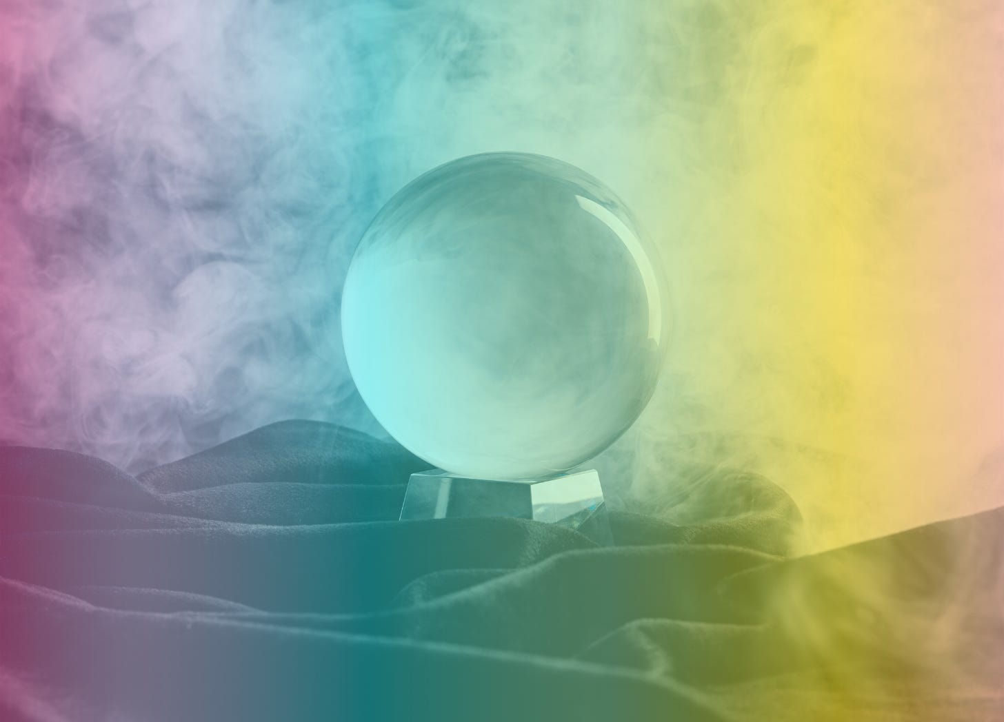 A rainbow-filtered image of a glass crystal ball sitting on a bed of black cloth and surrounded by white smoke