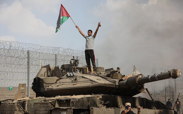 A Palestinian stands on an Israeli tank at the border fence near the city of Khan Younis in the southern Gaza Strip after some 3,000 Hamas terrorists burst through the border and entered Israel, slaughtering some 1,200 people, October 7, 2023. (Yousef Mohammed/Flash90)