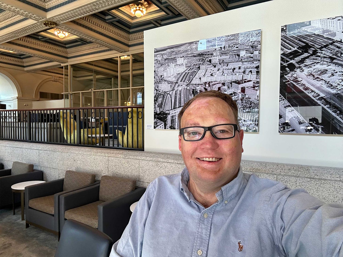 Selfie of John in the Amtrak lounge at Boston South Station, which has an ornate and timeless ceiling and a variety of seating areas.