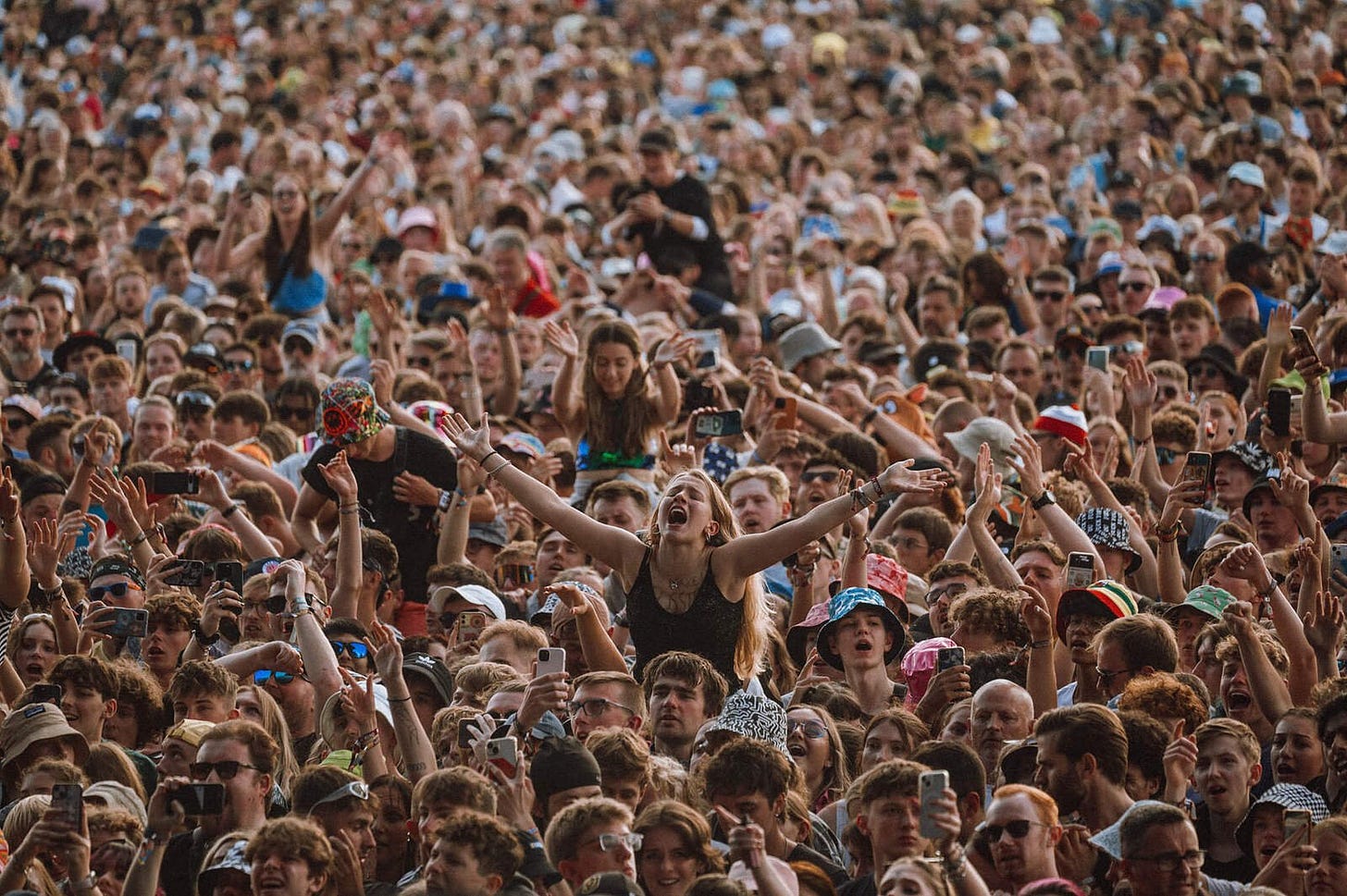 Huge crowd of fans at festival. Young woman in center has arms extended and is crying out in ecstasy