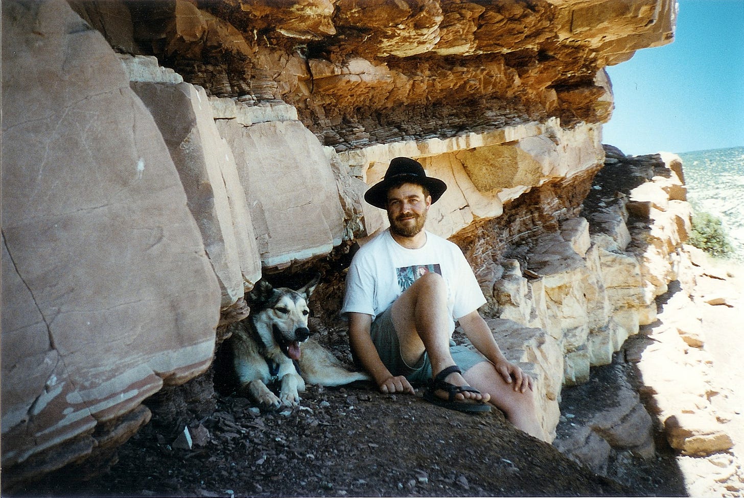 Extremely handsome dog and less handsome bearded 36-year-old Chris in the shade of a rock formation in utah.