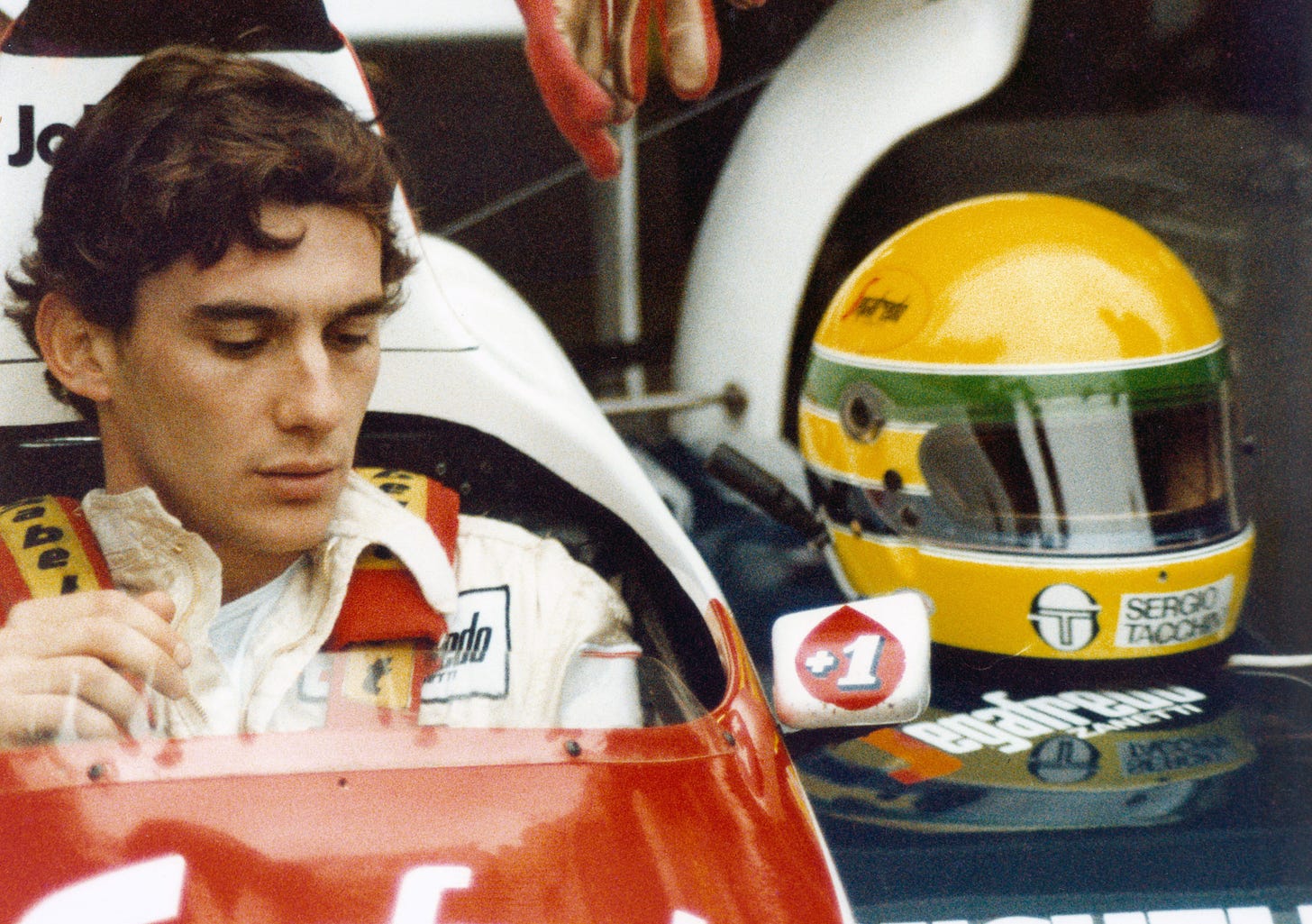 Still from the Senna documentary. F1 racecar driver Ayrton Senna sits in his car, helmet beside him.
