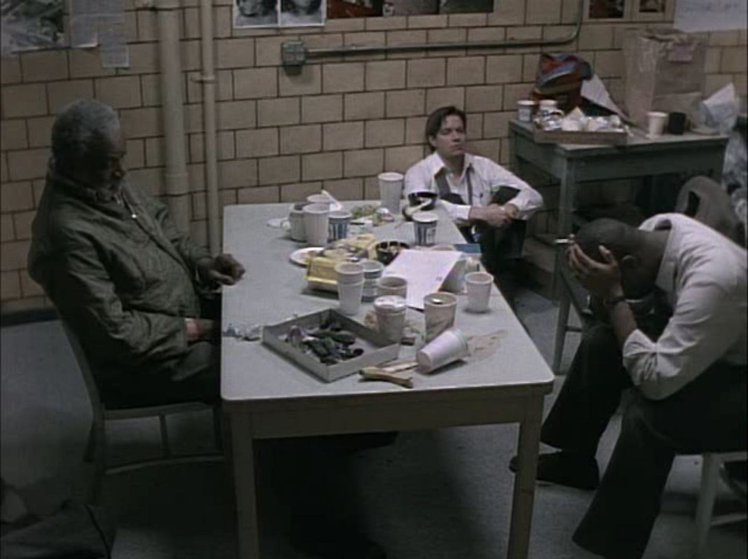 This still image from Homicide Life on the Street's Season 1 episode "Three Men and Adena" shows Risley Tucker (played by Moses Gunn), Tim Bayliss (played by Kyle Secor), and Frank Pembleton (played by Andre Braugher) spent, exhausted, and silent inside the Baltimore Homicide Unit's primary interrogation room. Tucker (on the left) sits at a table full of empty coffee cups, full ashtrays, and the detritus of several fast-food meals. Pembleton (on the right) sits in a chair with his head in his hands. Bayliss (center) sits with his back against a wall, staring at nothing. This still image from Homicide Life on the Street's Season 1 episode "Three Men and Adena" shows Risley Tucker (played by Moses Gunn), Tim Bayliss (played by Kyle Secor), and Frank Pembleton (played by Andre Braugher) spent, exhausted, and silent inside the Baltimore Homicide Unit's primary interrogation room. Tucker (on the left) sits at a table full of empty coffee cups, full ashtrays, and the detritus of several fast-food meals. Pembleton (on the right) sits in a chair with his head in his hands. Bayliss (center) sits with his back against a wall, staring at nothing.