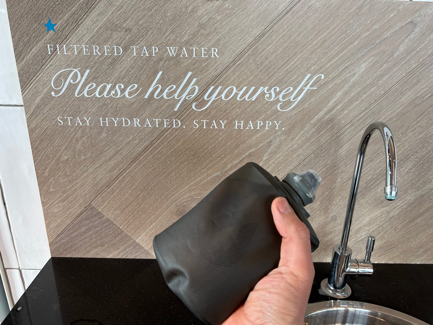 An image of my hand holding a flexible water bag full of fresh drinking water infant of a free drinking water fountain at Pret at the Rugby Services.