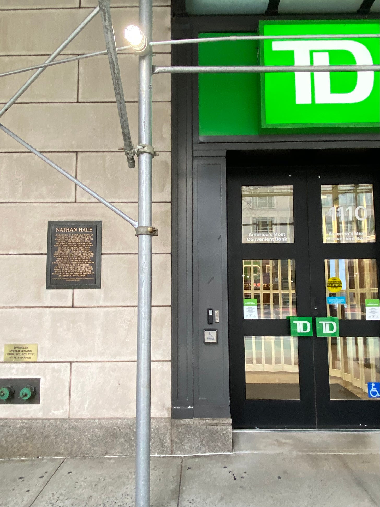 The entrance of a TD Bank covered in scaffolding with a plaque that has NATHAN HALE written on top in all caps.