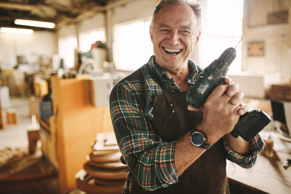 Elder man holding power drill, excited to get started on a new woodworking project.