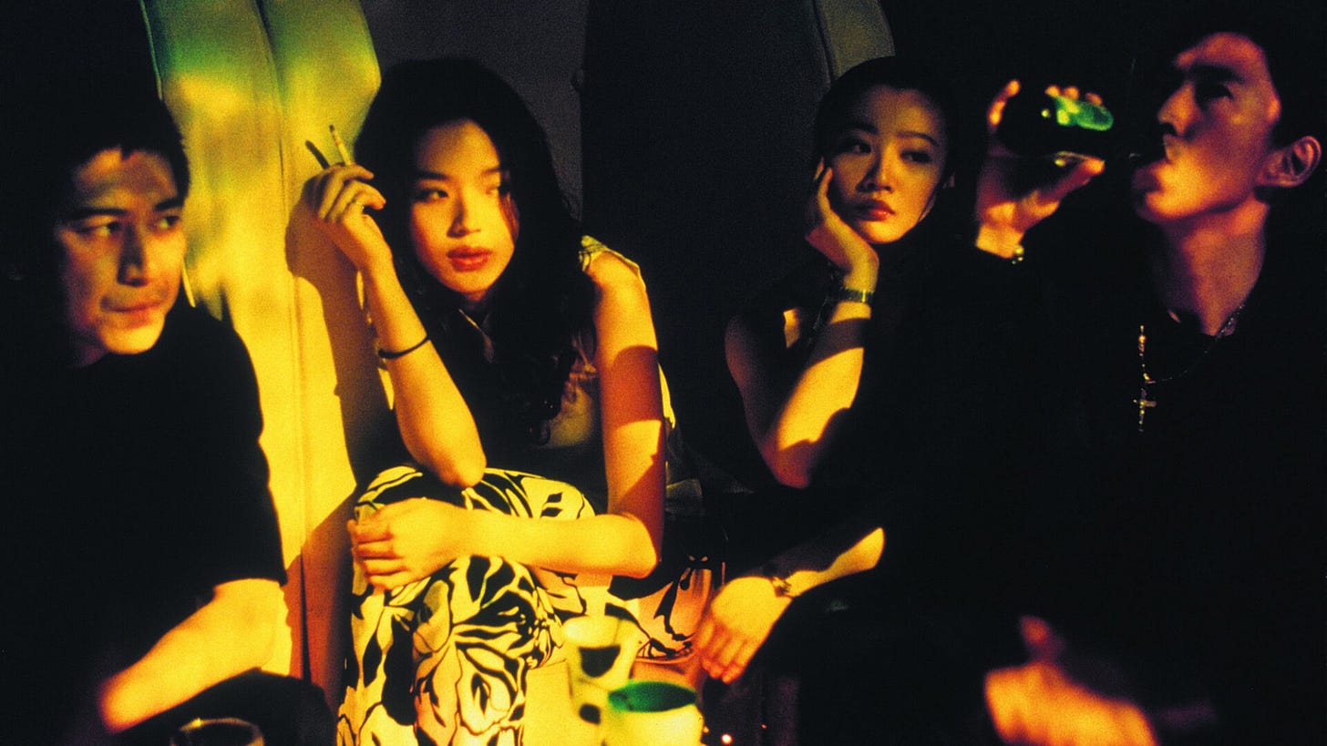 Movie still from Millennium Mambo. Two young women and two young men sit in a dark bar with cigarettes and drinks.