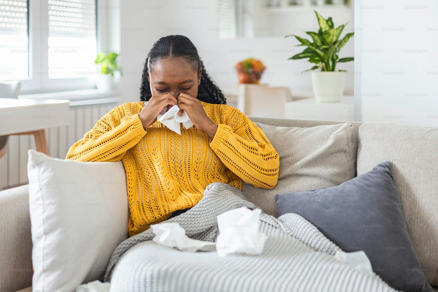 Sick young african woman feeling cold covered with blanket sit on bed, ill black girl shivering freezing warming at home wrapped with plaid, no central heating problem, fever temperature flu concept