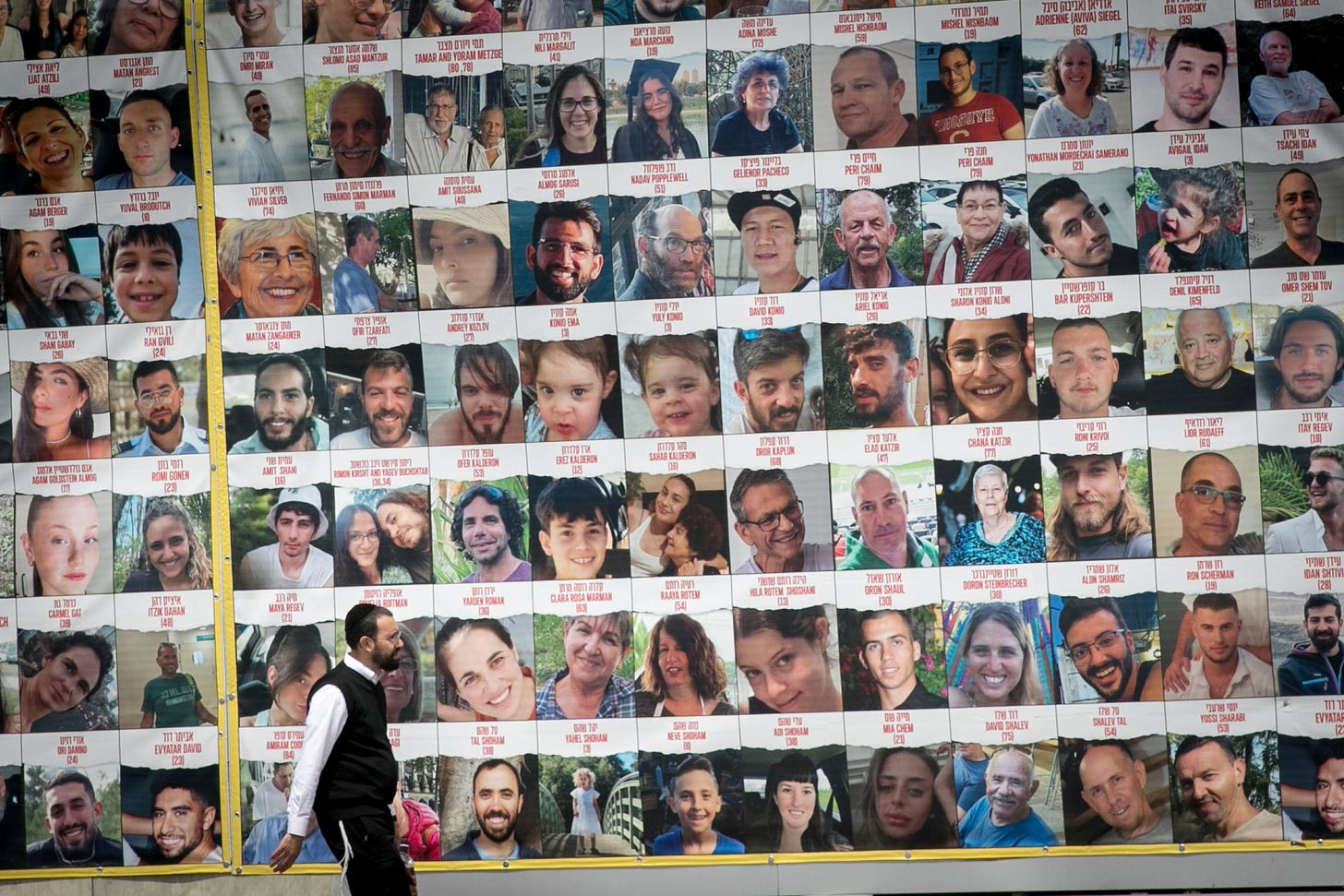People walk by photographs of Israelis held hostage by Hamas in Gaza, in Tel Aviv, April 9, 2023. (Miriam Alster/Flash90)