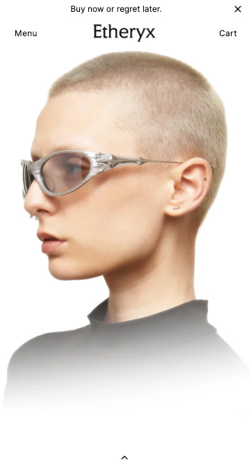 A head-and-shoulders profile shot of a person with a shaved head and light skin wearing futuristic silver sunglasses. They have a nose ring and a small stud earring. The background is a gradient from white at the top to a blurry light gray at the bottom. The text "Etheryx" is centered at the top of the image between "Menu" and "Cart" links. A small up arrow is at the bottom of the image. The phrase "Buy now or regret later" is at the very top.