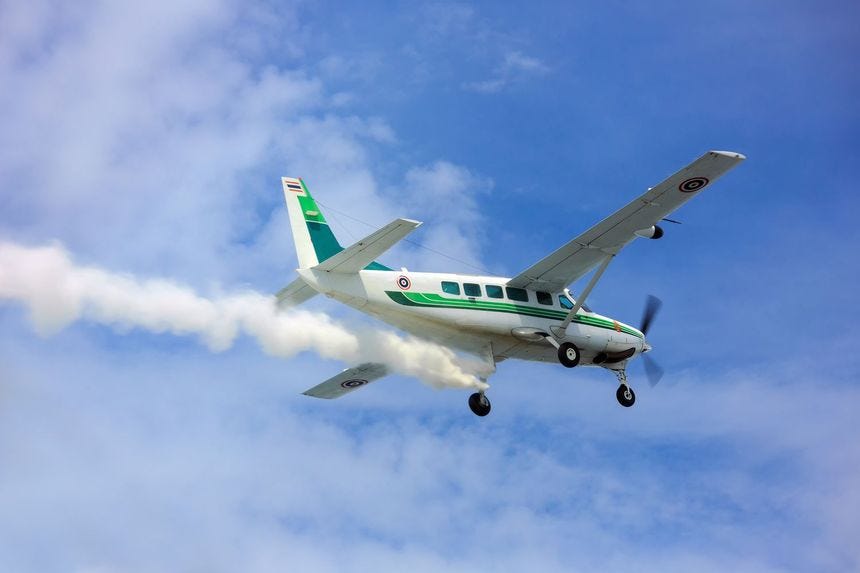 Close-up of a turboprop plane sprinkling chemicals into clouds in a blue sky.