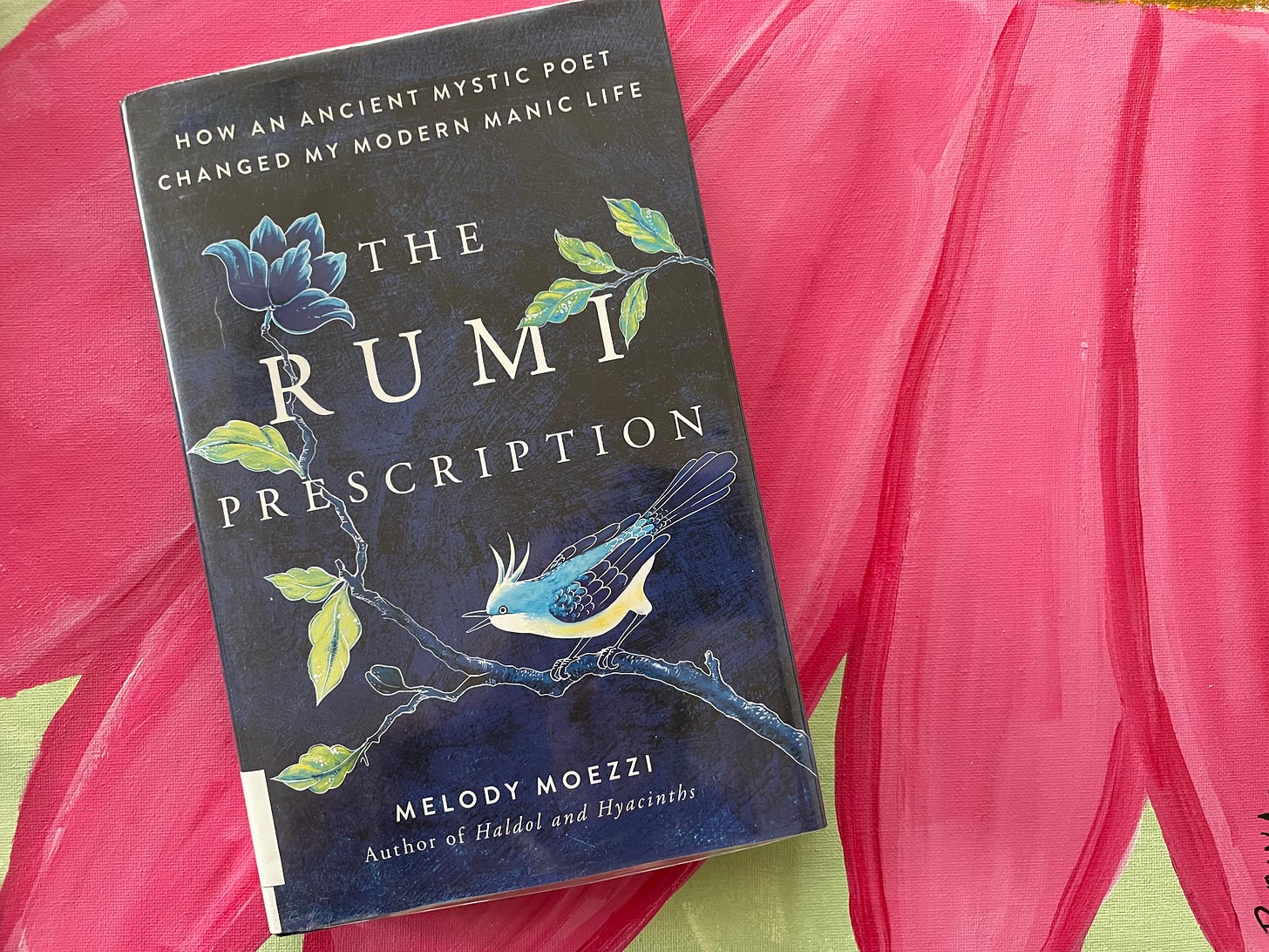 A copy of The Rumi Prescription, a dark blue book with hummingbirds, branches, leaves, and flowers on the cover. Behind the book is a hot pink painting of flower petals.