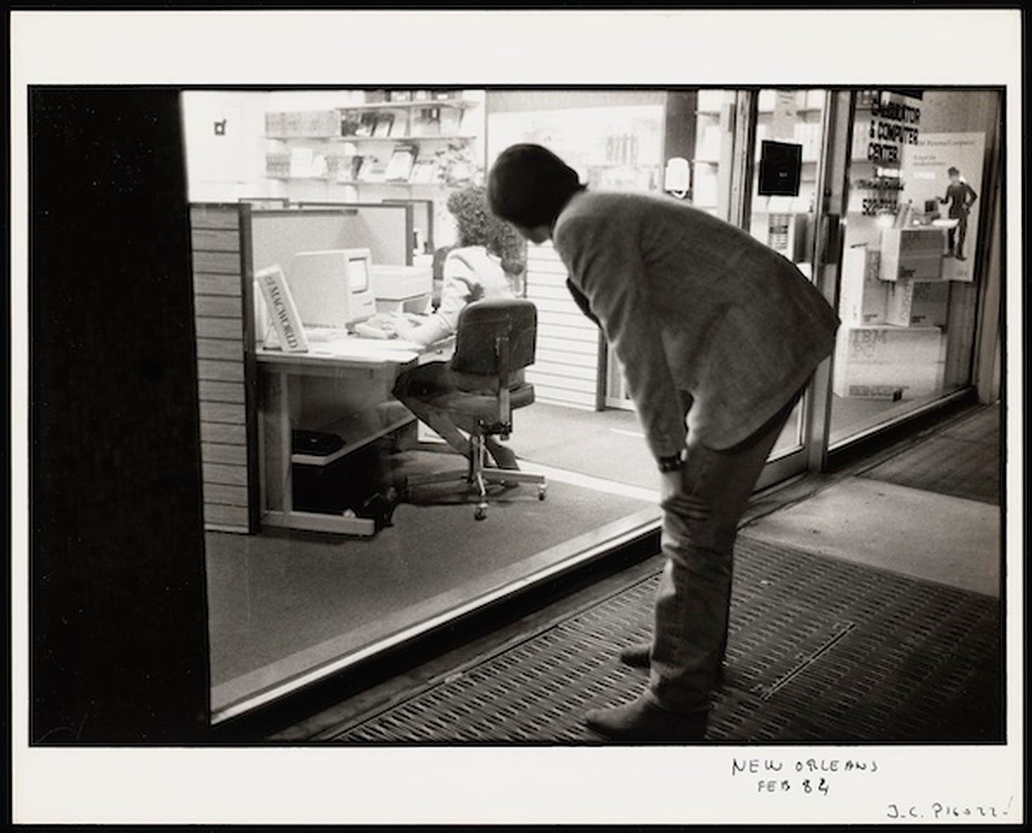 A photo of Steve Jobs looking at somebody using a Macintosh.