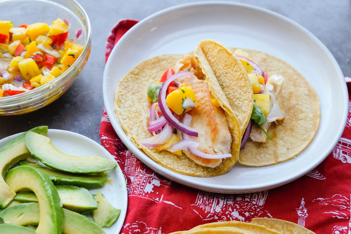 Fish Tacos with tropical fruit sals and sliced avocados on a white plate