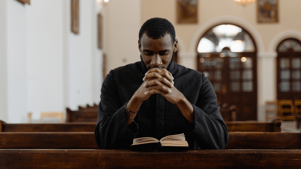 man praying at a church pew with an open Bible