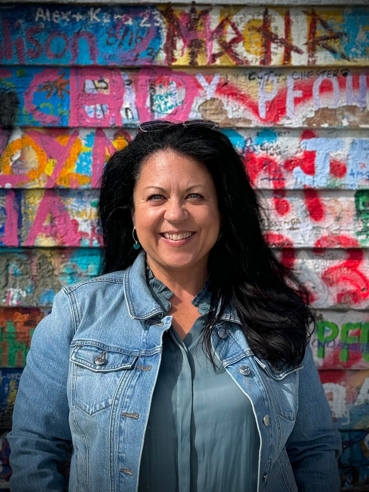 Rebecca Blackwell with dark hair wearing a blue top. Stood in front of a multicoloured wall.