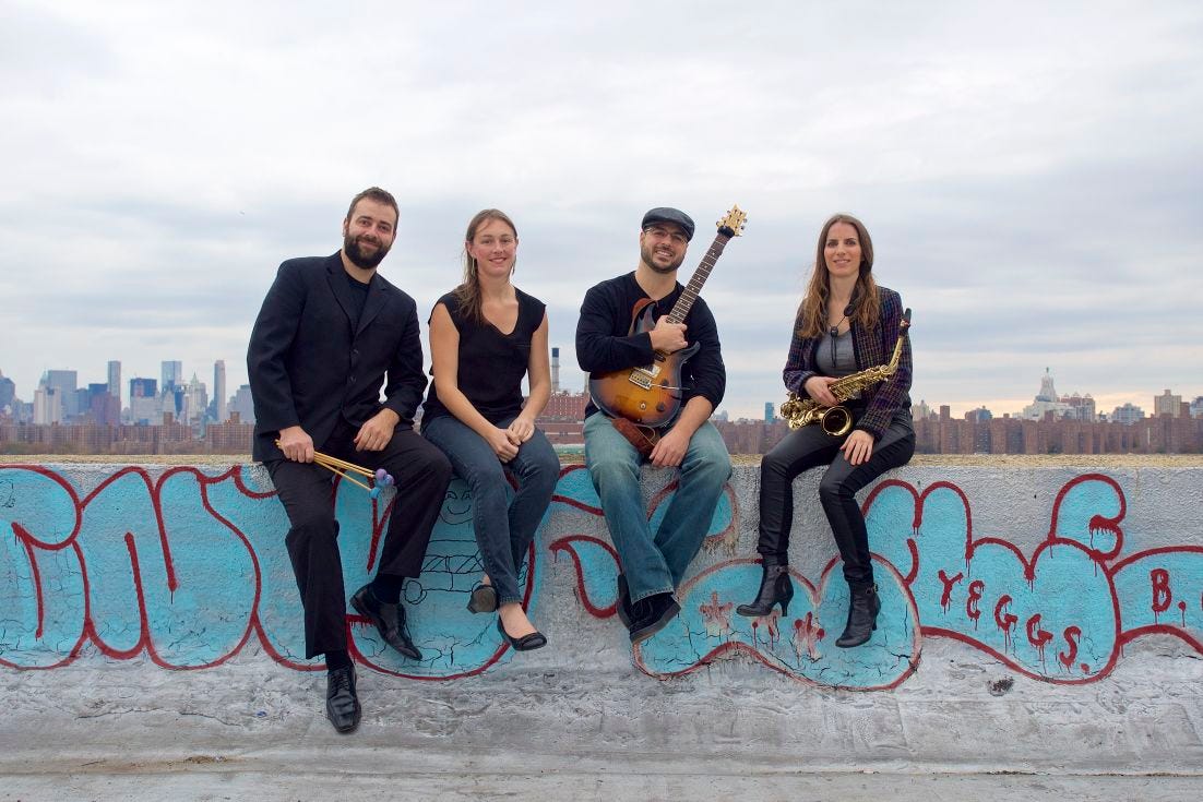 Four musicians sitting on a stone wall with graffiti, city skyline in background