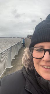 A selfie. Me in a bobble hat, with a grey River Mersey in the background.