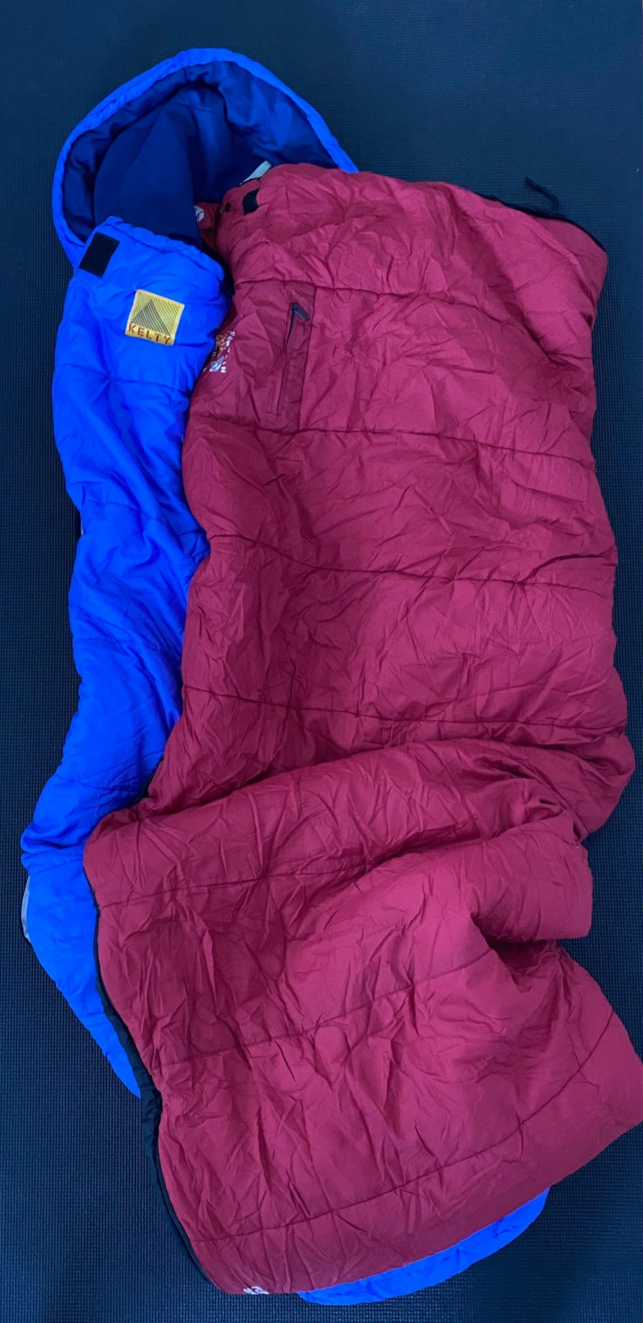 One blue sleeping bag and one red sleeping bag on black yoga mat.