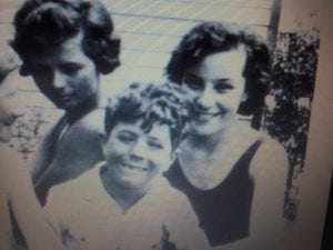 Two teen girls and a boy smile for the camera in a black and white photo