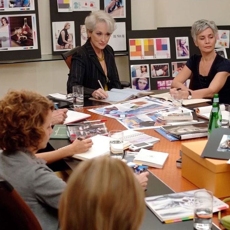 This may contain: three women sitting at a table with books and magazines on it, surrounded by other people