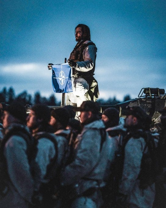 Swedish armoured troops from the South Scanian Regiment gather at dusk, with one soldier holding the NATO flag. 

Photo: 7 March 2024, David Kristiansen / Swedish Armed Forces 