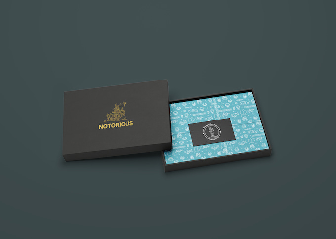 A black two-piece box with a gold foil logo on the cover. The box is open and shows blue custom tissue paper inside.