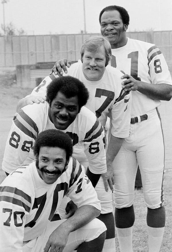 A black and white photo of the four huddled together wearing white Viking uniforms without helmets on. 
