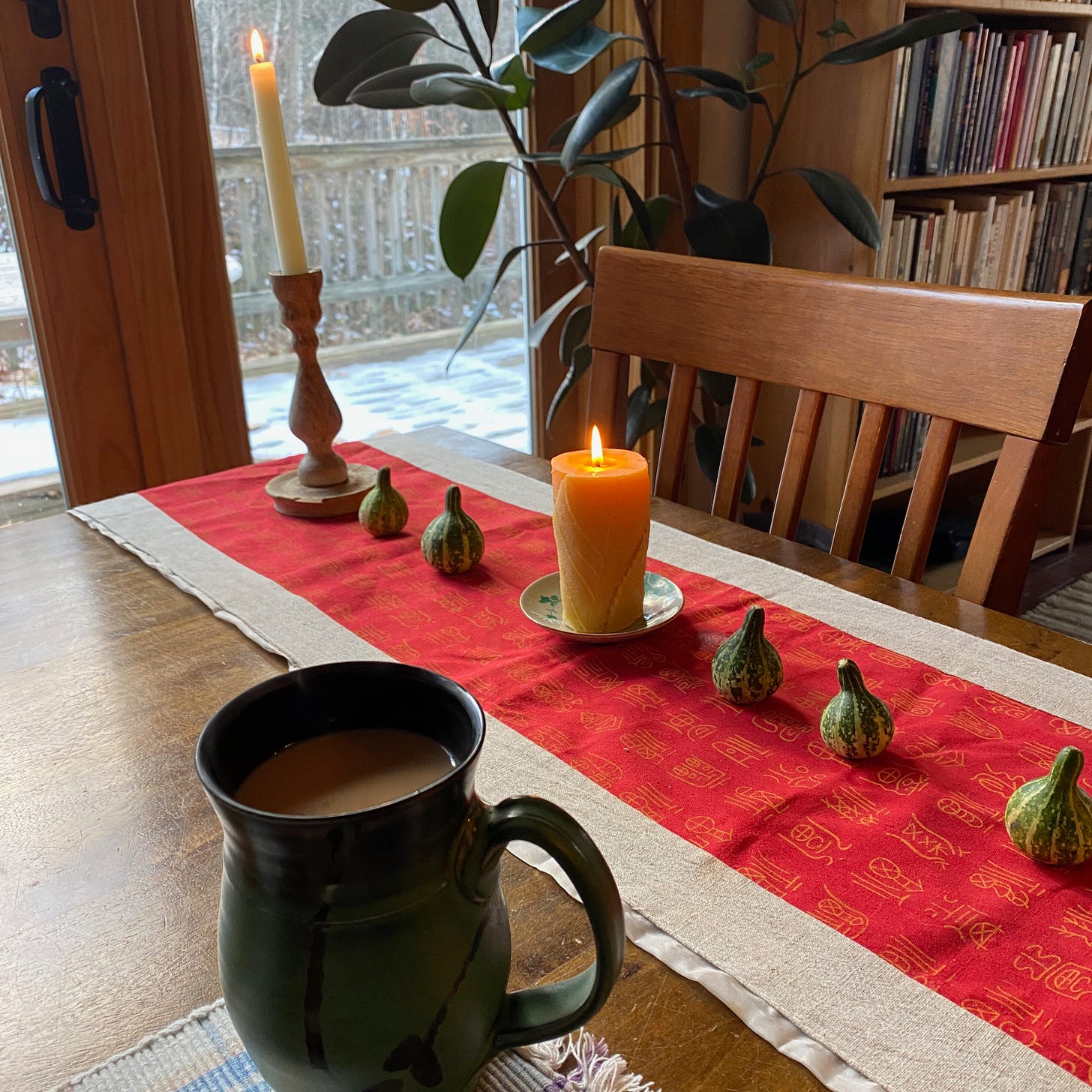 A mug of tea sitting on a table next to several lit candles on a red cloth.