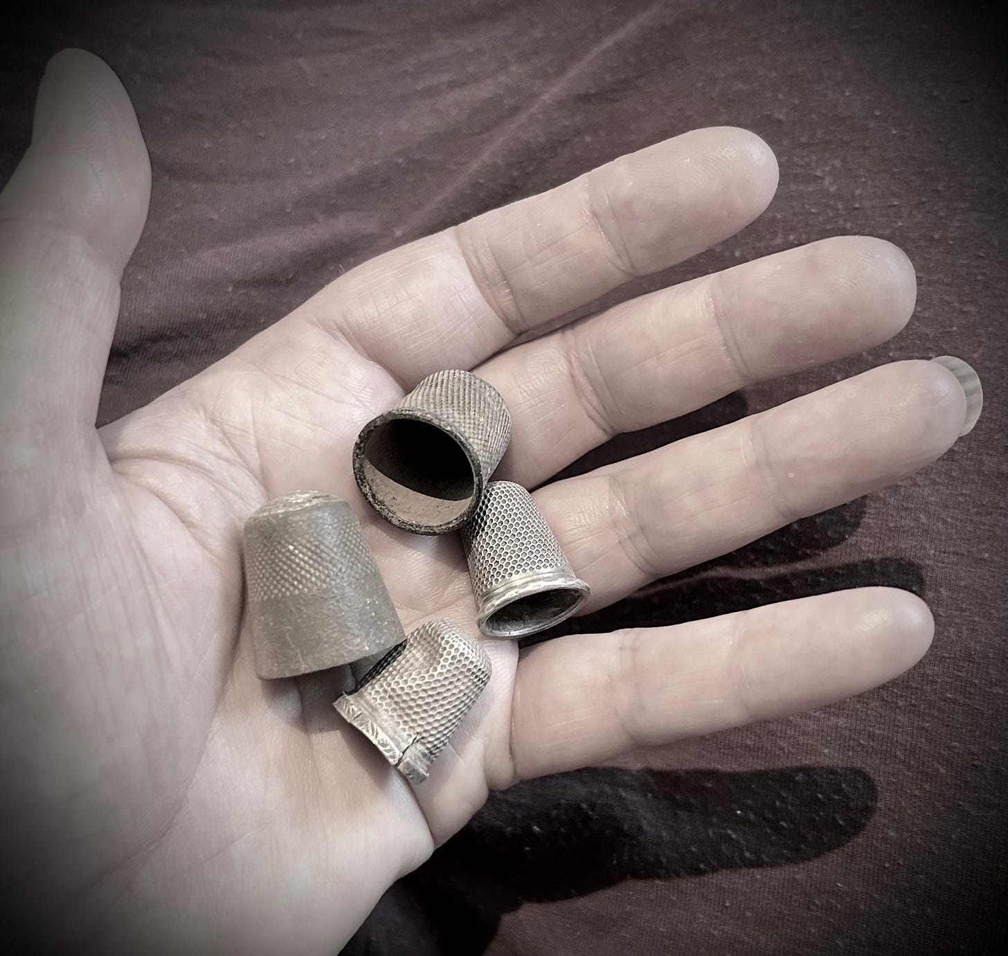 A hand holding four old thimbles, which are dusty with dry earth