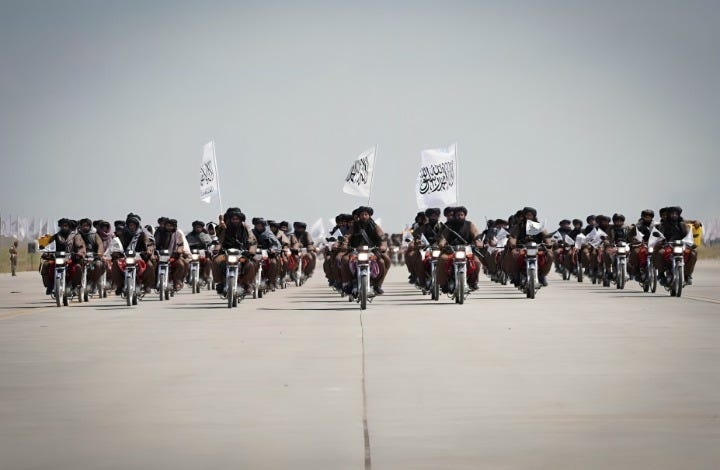 Taliban fighters on motorcycles with flags, riding in formation.