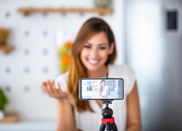 a woman recording a video of herself via a mobile phone propped up on a tripod