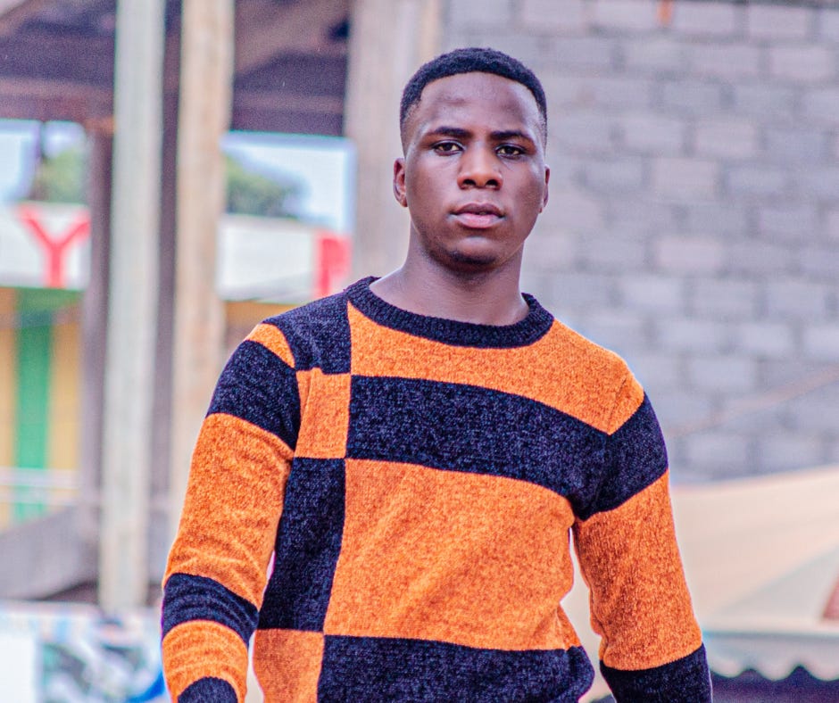 A young person wearing a blue and orange sweater stares directly at the camera and appears to be walking on a street.